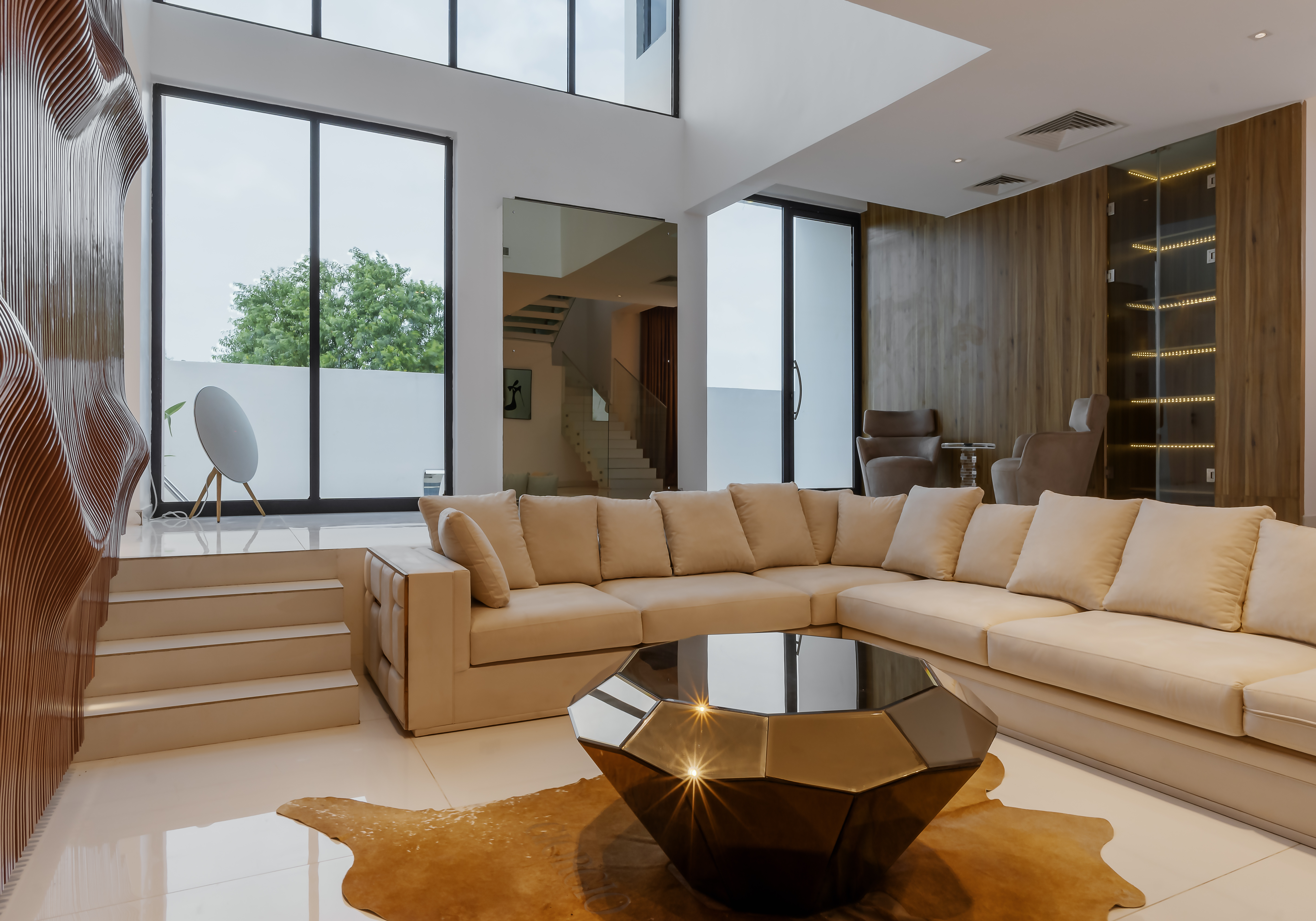 Living room at Ilé Bash with a cream sectional sofa, faceted bronze coffee table and sculptural timber feature wall